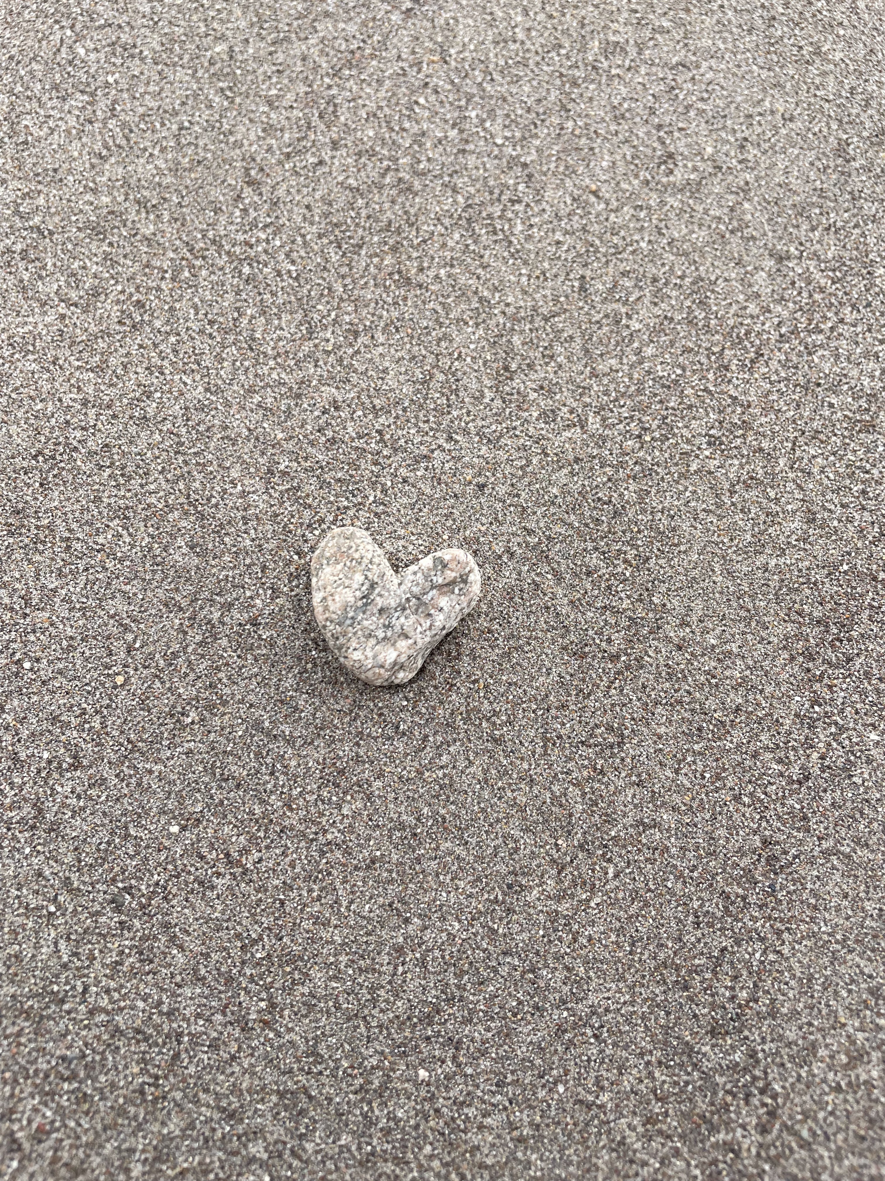 A small heart-shaped stone resting on soft sand